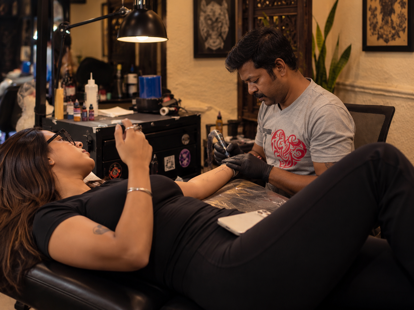 A tattoo artist works on a client’s arm while she lies comfortably in a professional tattoo studio.