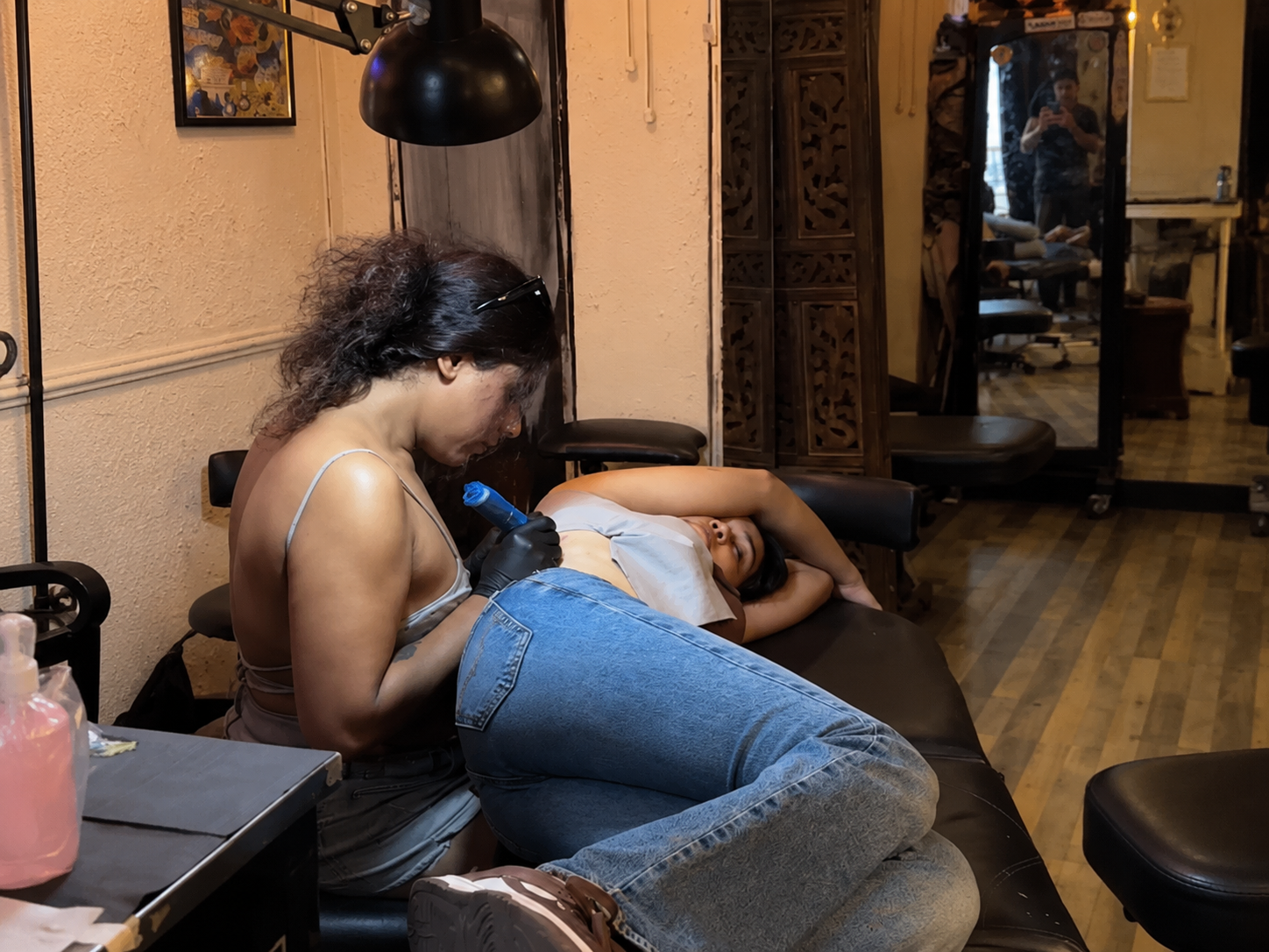 A tattoo artist works on a client lying on a tattoo bed inside a professional tattoo studio.