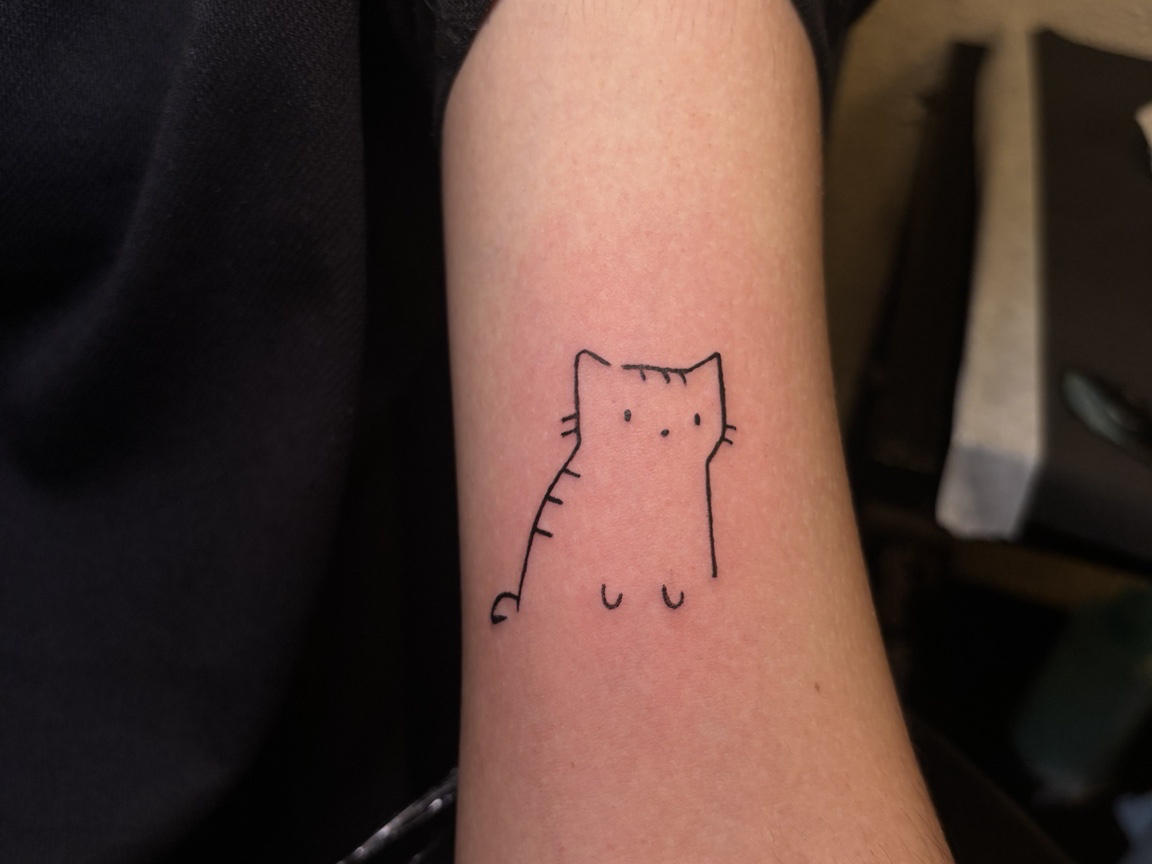 A small minimalist cat tattoo in fine black linework on a person’s forearm.