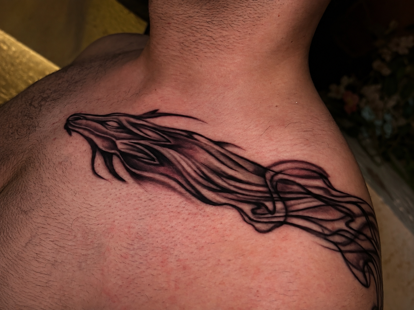 Close-up of a black and grey abstract tattoo flowing across a person’s upper chest and shoulder.