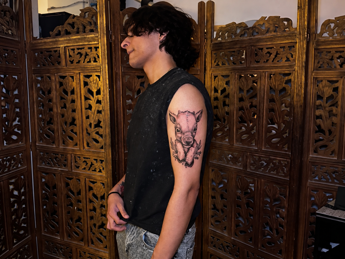 Young man showing a detailed piglet tattoo with leafy accents on his upper arm inside a tattoo studio.