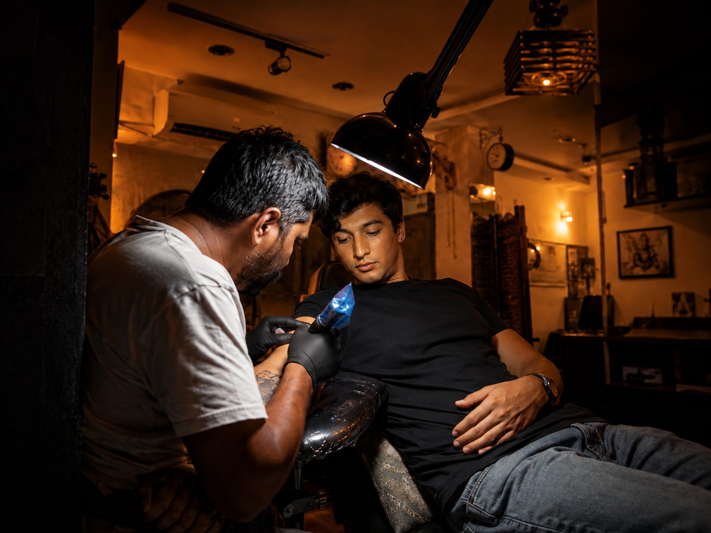 Tattoo artist working on a client's forearm inside a warm, atmospheric tattoo studio