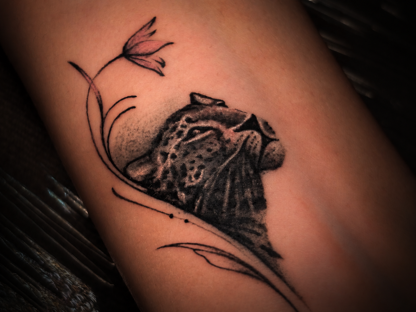 Close-up tattoo featuring a detailed big cat portrait framed by delicate botanical linework on the skin.