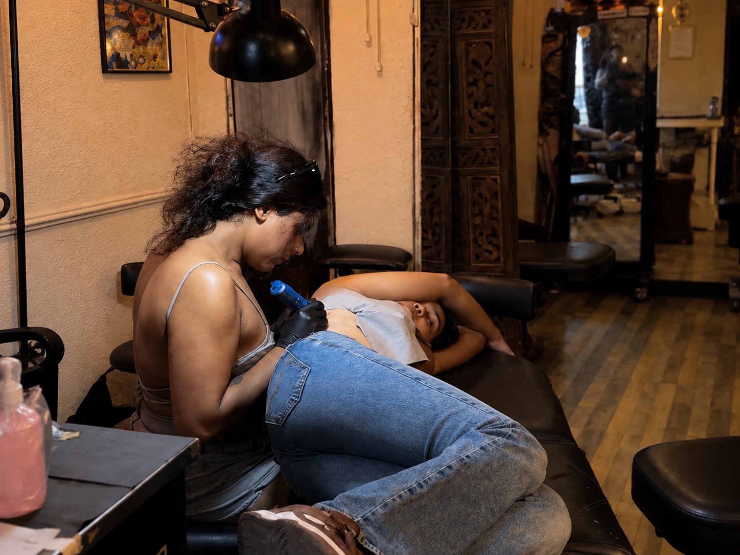 A tattoo artist working on a client during a private tattoo session in a warm, intimate studio.