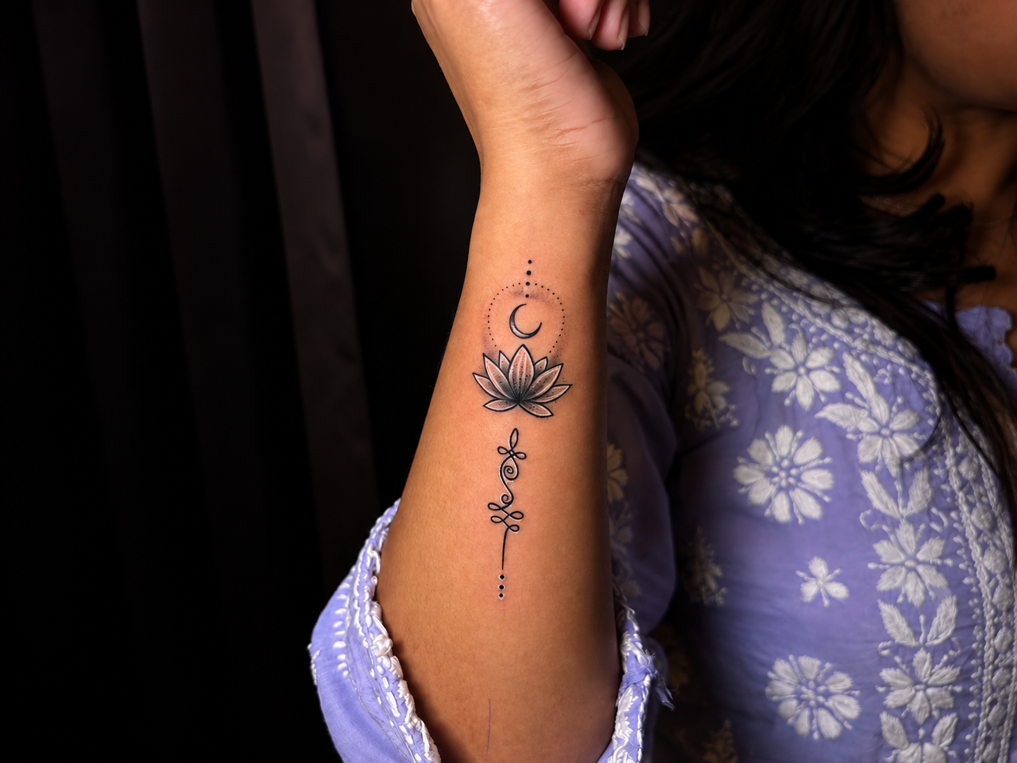 Close-up of an elegant black and grey lotus and crescent moon tattoo with delicate ornamental detailing on the inner forearm.