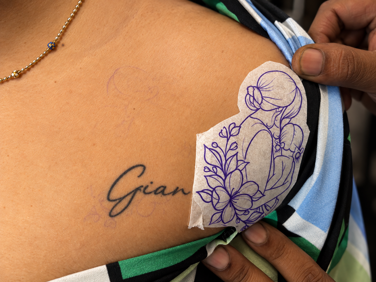 Close-up of a tattoo cover-up process on the upper chest, showing an existing name tattoo alongside a floral female figure stencil prepared for a new design.