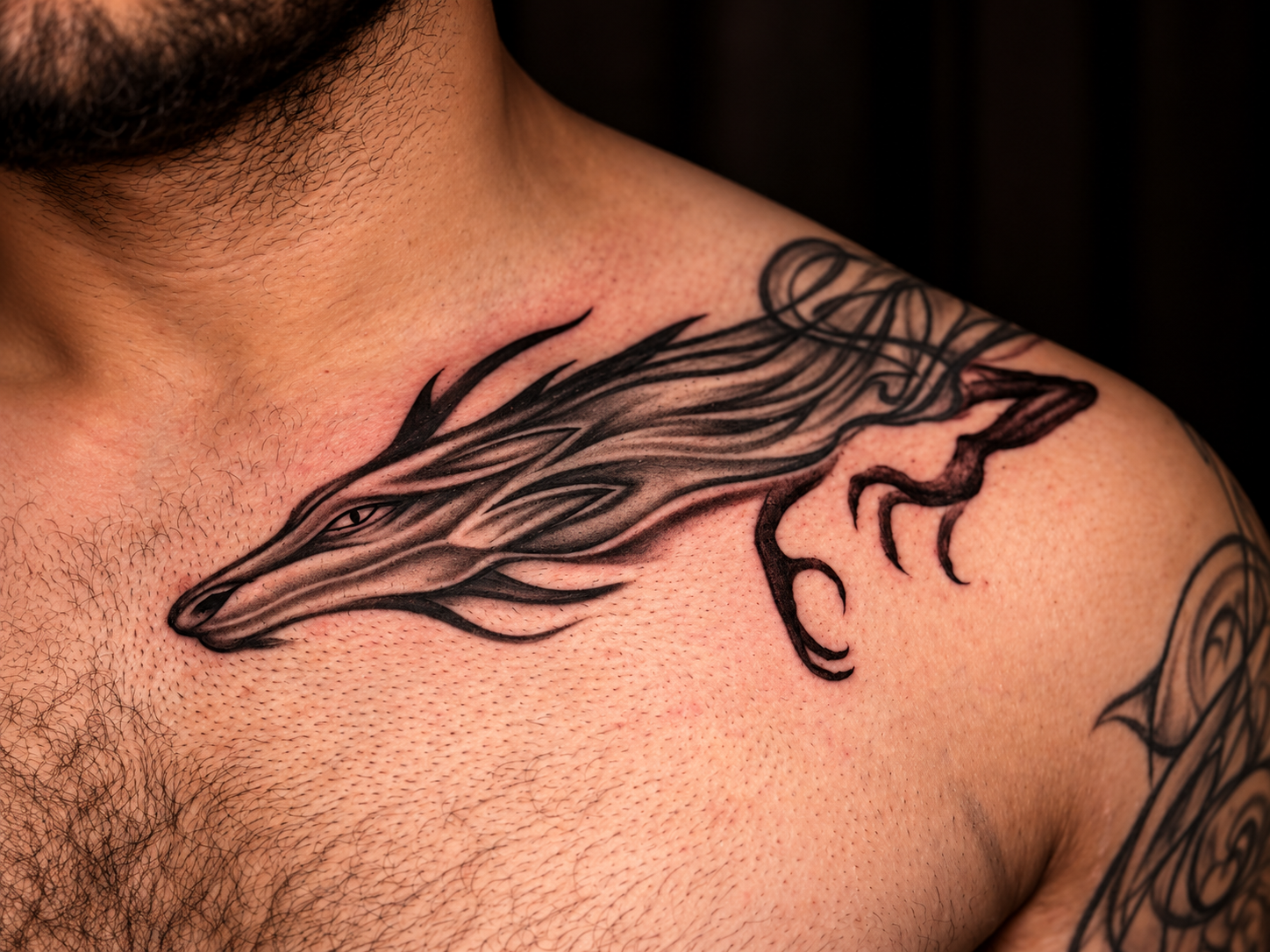 Close-up of a black and grey wolf-inspired tattoo extending from the collarbone across the shoulder, with flowing lines and detailed shading.