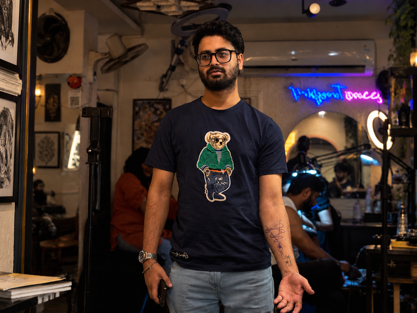 Tattoo client standing inside a professional tattoo studio with a tattoo artist working in the background, highlighting the importance of choosing a tattoo studio beyond price alone.