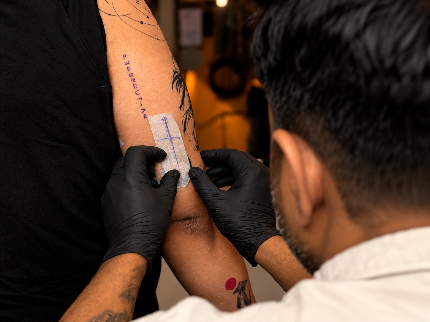 Tattoo artist applying a stencil to a client’s upper arm while refining the placement of a new tattoo design inside a professional tattoo studio.