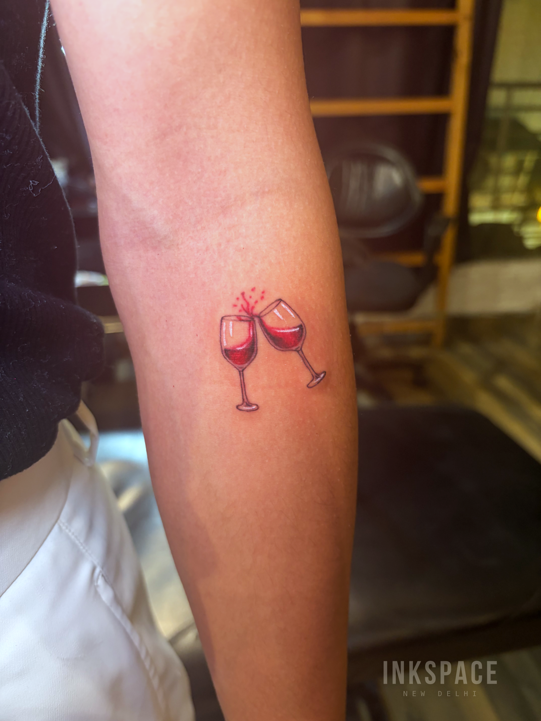 Detailed fine line tattoo of two wine glasses on skin
