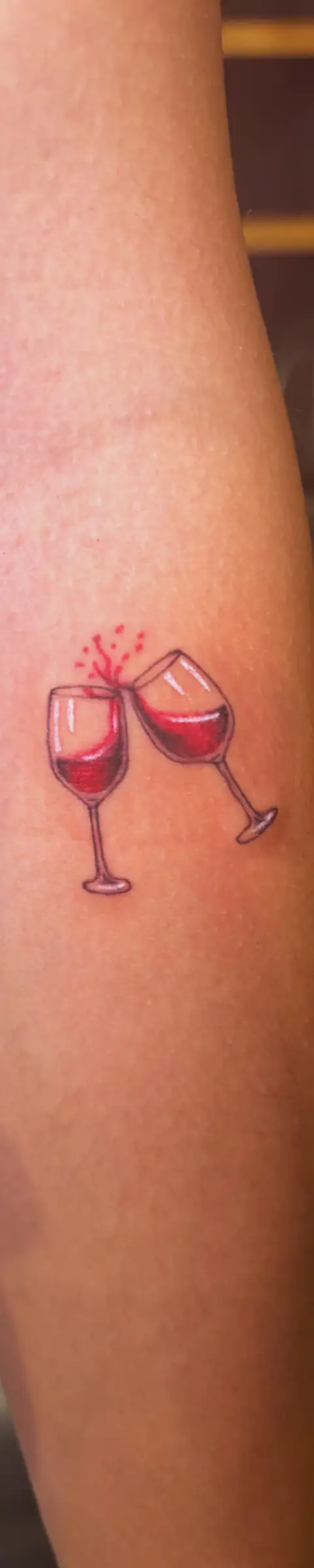 Detailed fine line tattoo of two wine glasses on skin