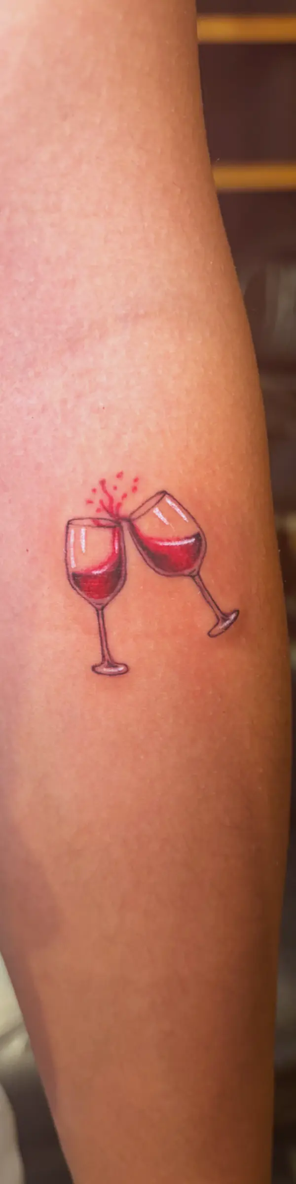 Detailed fine line tattoo of two wine glasses on skin