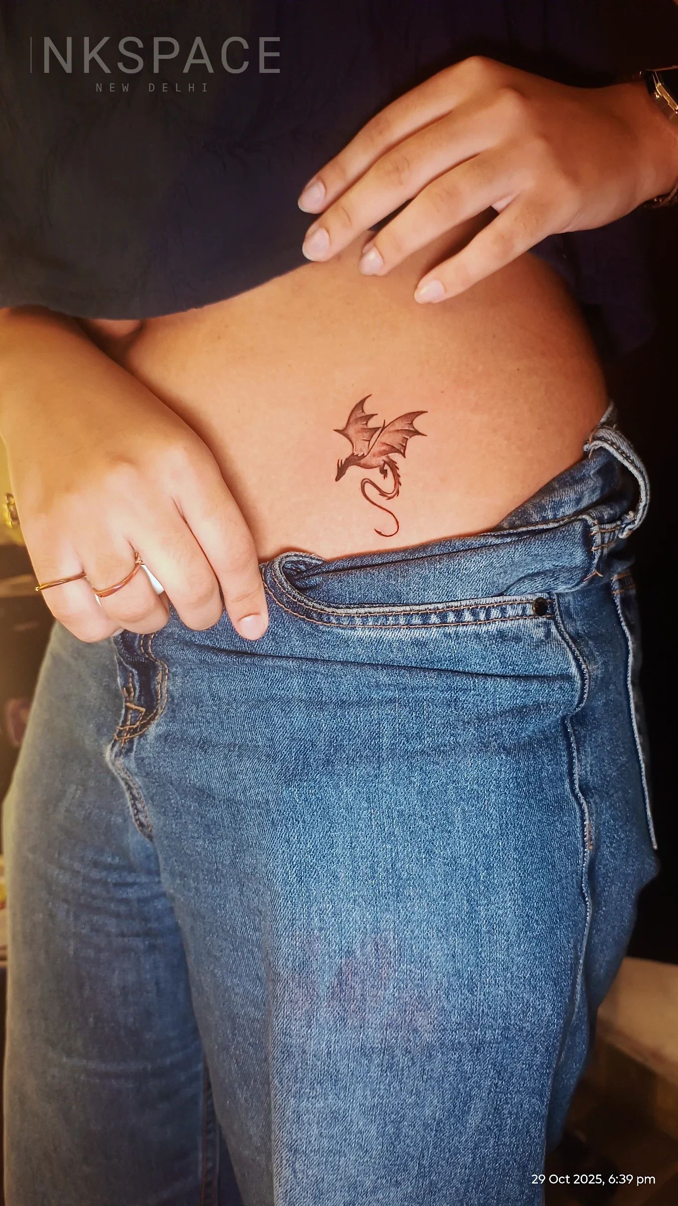 A delicate, illustrative dragon tattoo rendered in warm, earthy tones on the lower abdomen.