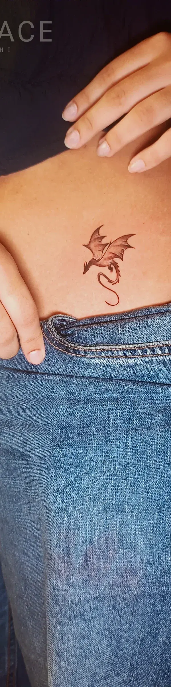 A delicate, illustrative dragon tattoo rendered in warm, earthy tones on the lower abdomen.